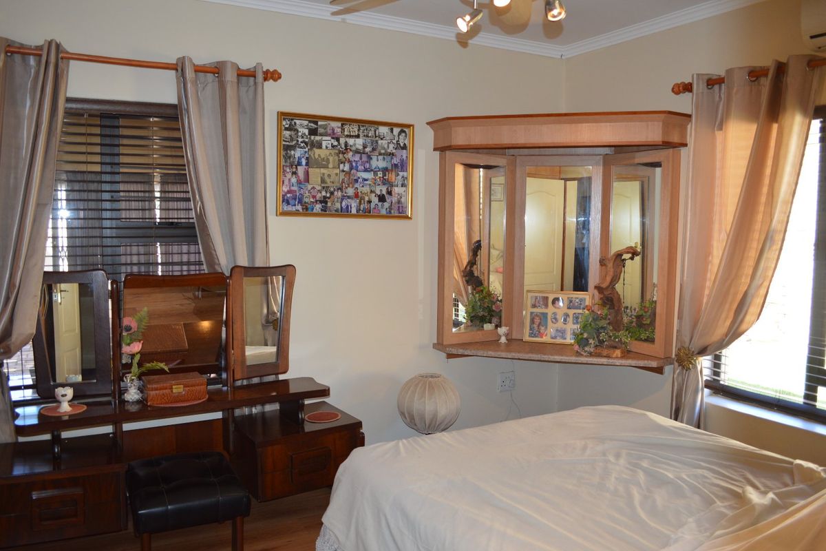 A bedroom featuring a built-in vanity unit, ceiling fan, and dual windows with venetian blinds.
