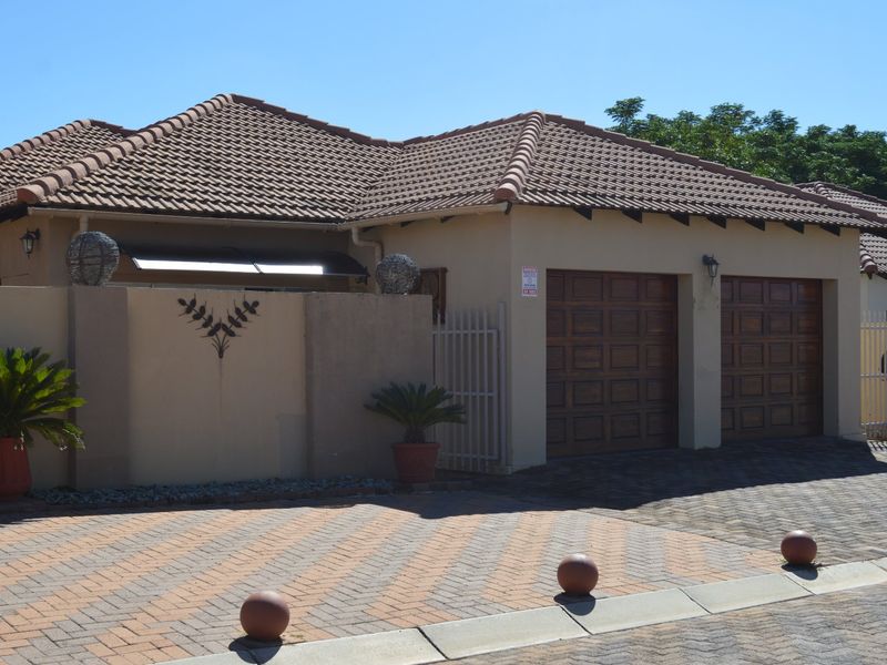 Front elevation of a townhouse featuring a double garage, paved driveway, and secure boundary wall with tiled roof.