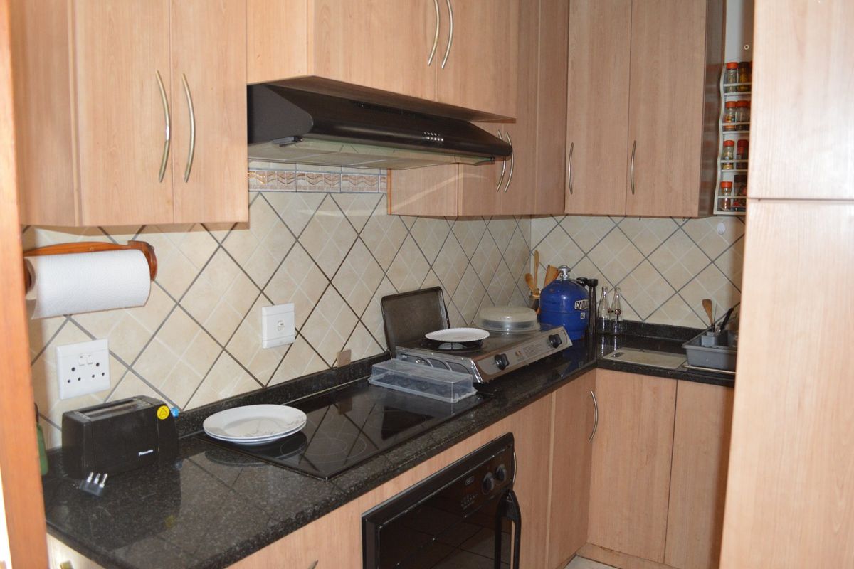 A compact kitchen featuring laminate cabinetry, granite countertops, a built-in oven, and a ceramic hob with a tiled backsplash.