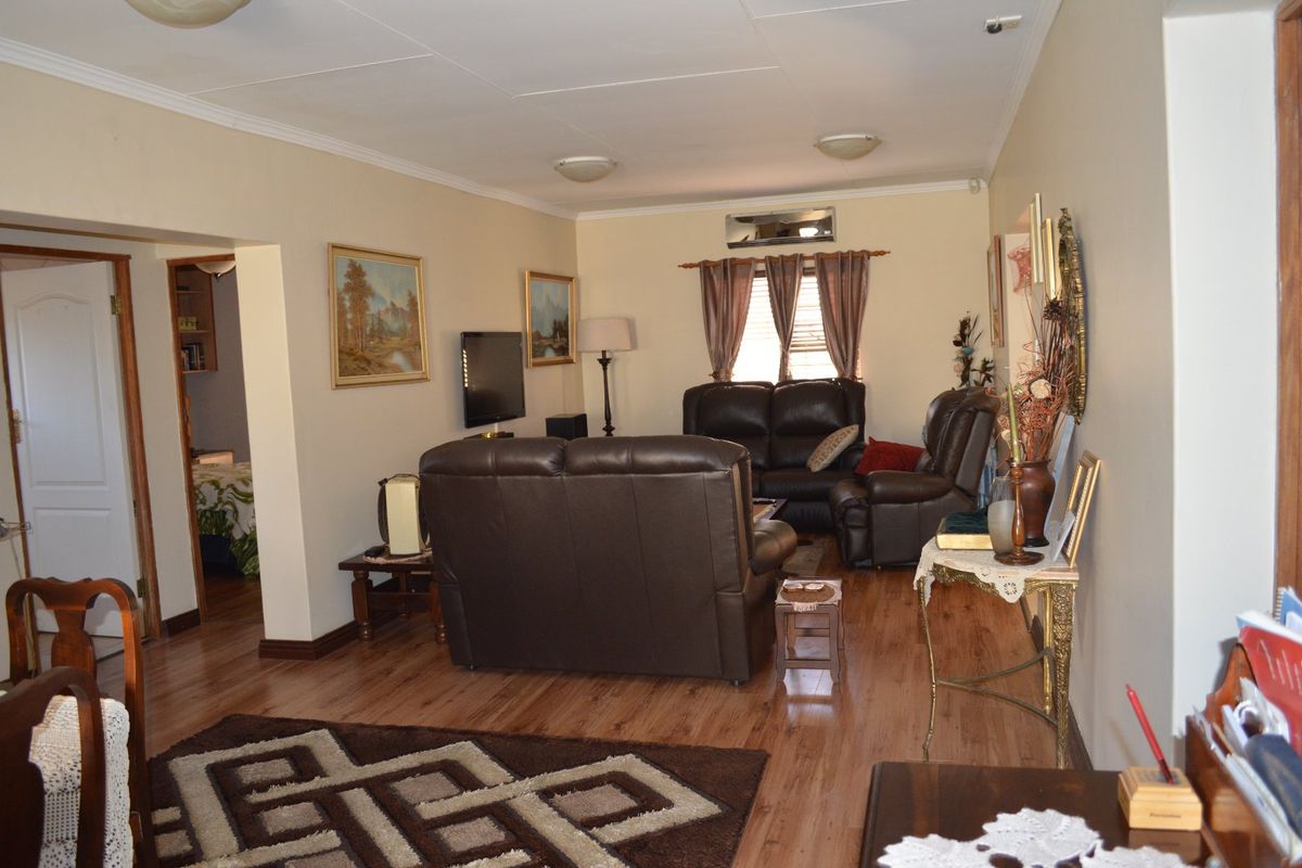 A comfortable living room featuring laminate flooring, coved ceilings, and a wall-mounted air conditioning unit, providing a functional and well-maintained living space.