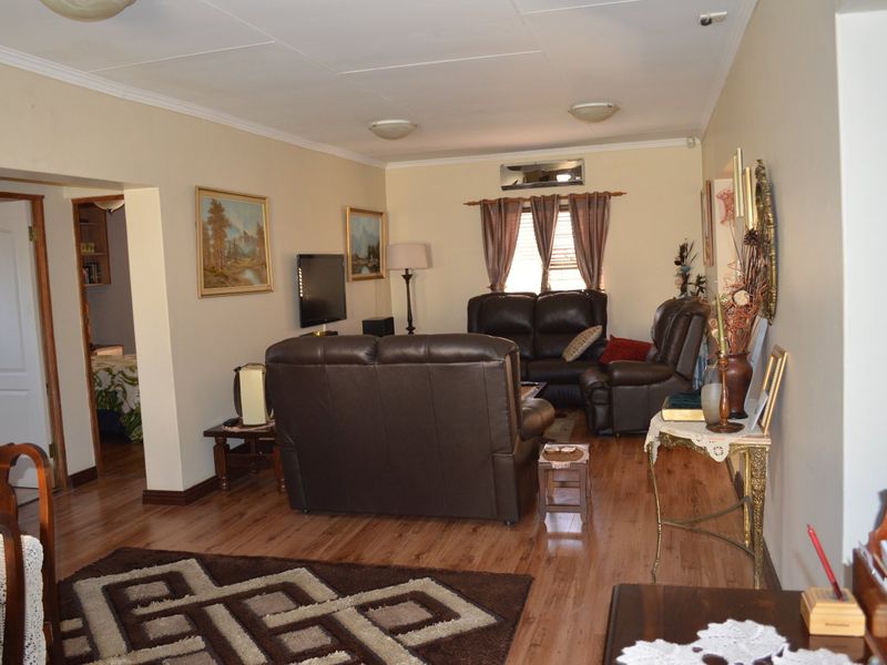 A comfortable living room featuring laminate flooring, coved ceilings, and a wall-mounted air conditioning unit, providing a functional and well-maintained living space.