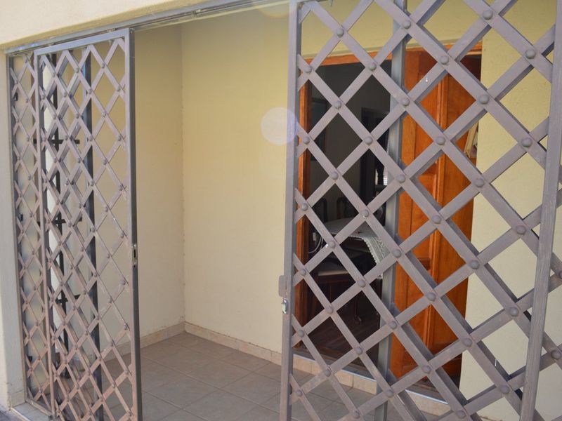 A covered patio area featuring tiled flooring and a metal security gate, providing access to the interior living space.
