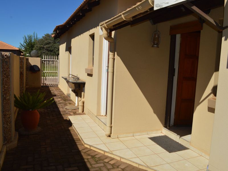 Rear exterior view of the townhouse featuring a paved walkway, tiled patio area, and an external utility sink.