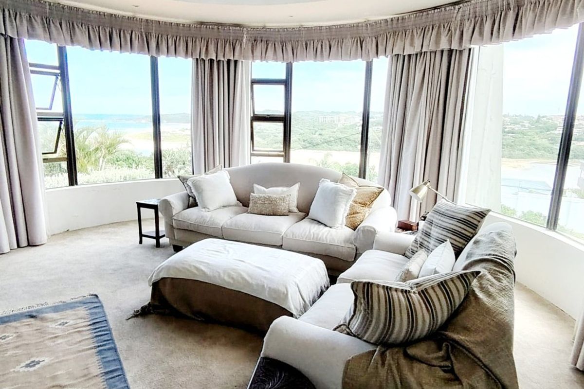 A spacious living room featuring a curved wall of windows with panoramic views, a decorative ceiling mural, and a central chandelier.