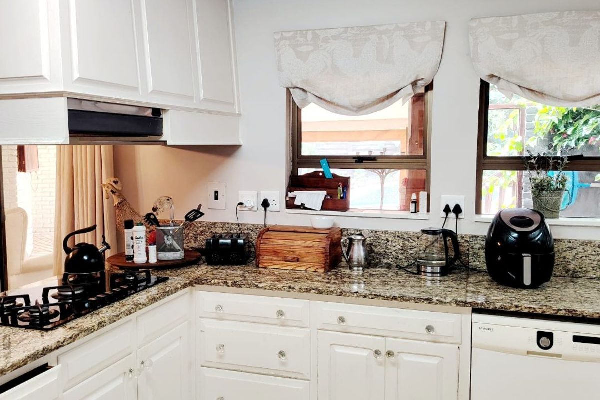 A functional kitchen featuring white cabinetry, granite countertops, a gas hob with extractor fan, and exposed timber ceiling beams.