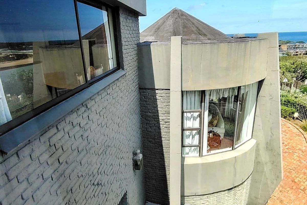 An elevated view of the rear exterior featuring unique architectural design with curved brick walls, a conical roof, and a paved patio area.