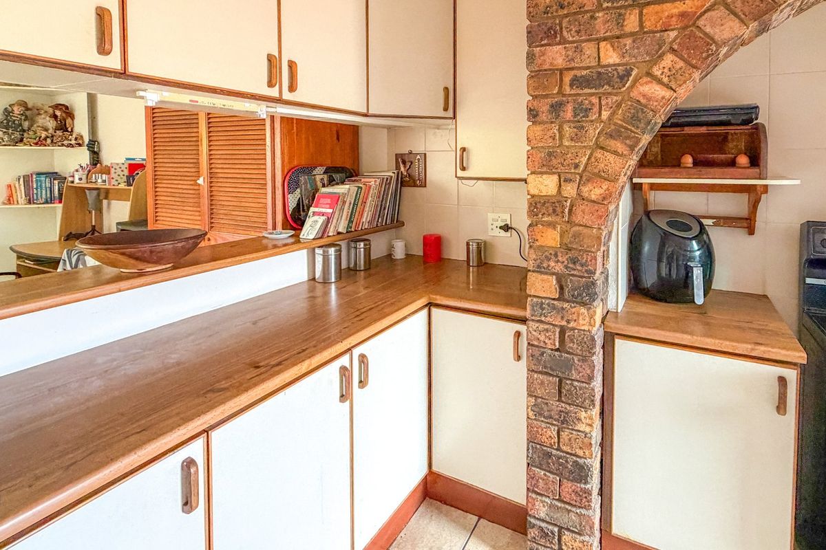 A functional kitchen featuring laminate countertops, built-in cabinetry, and a distinctive brick archway, offering a classic layout with potential for modern updates.