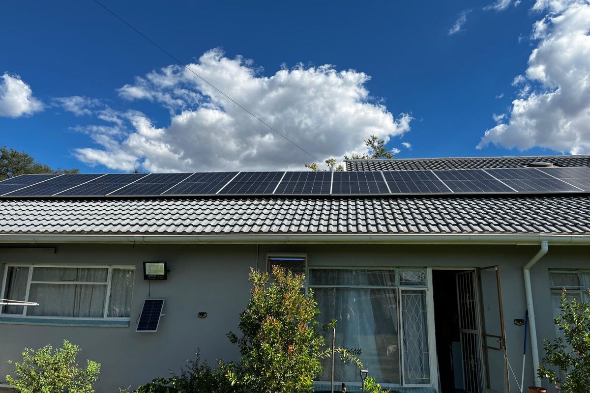 Rear exterior view of the house featuring a tiled roof equipped with a large array of solar panels and aluminum window frames.