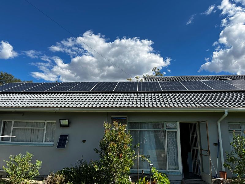 Rear exterior view of the house featuring a tiled roof equipped with a large array of solar panels and aluminum window frames.