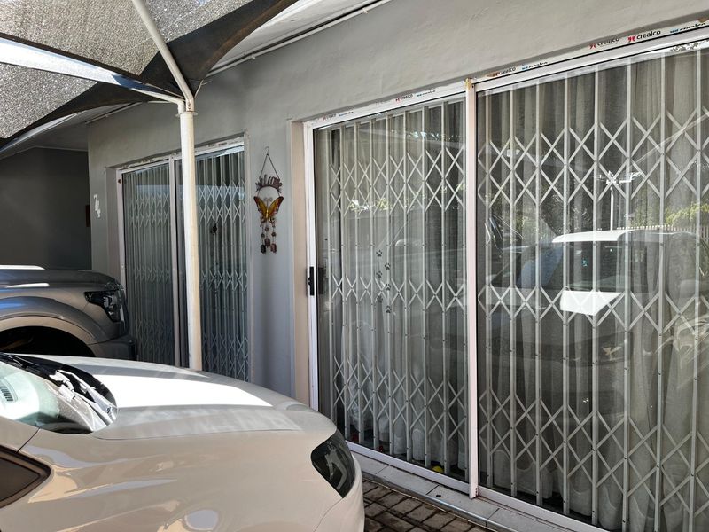 Front exterior view featuring sliding glass doors with security gates and a shade sail covering the paved driveway area.