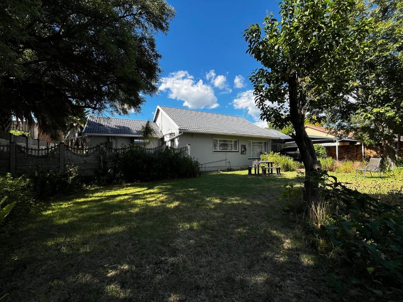 Rear view of the house featuring a tiled roof, established garden with mature trees, and a precast concrete boundary wall.