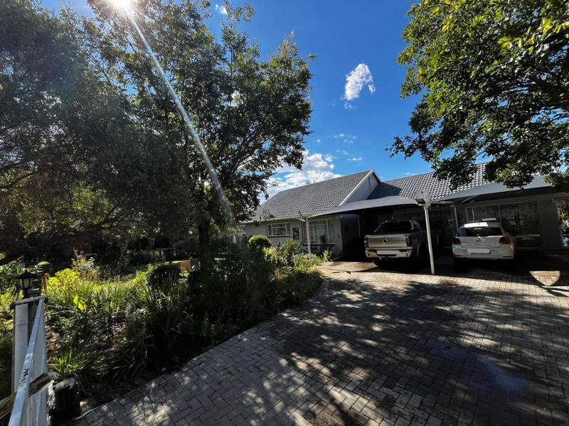 Front view of the property featuring a paved driveway, a double carport, and a well-established garden area.