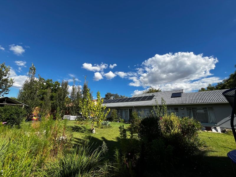 Rear view of the property featuring a well-maintained garden, tiled roof, and installed solar panels.