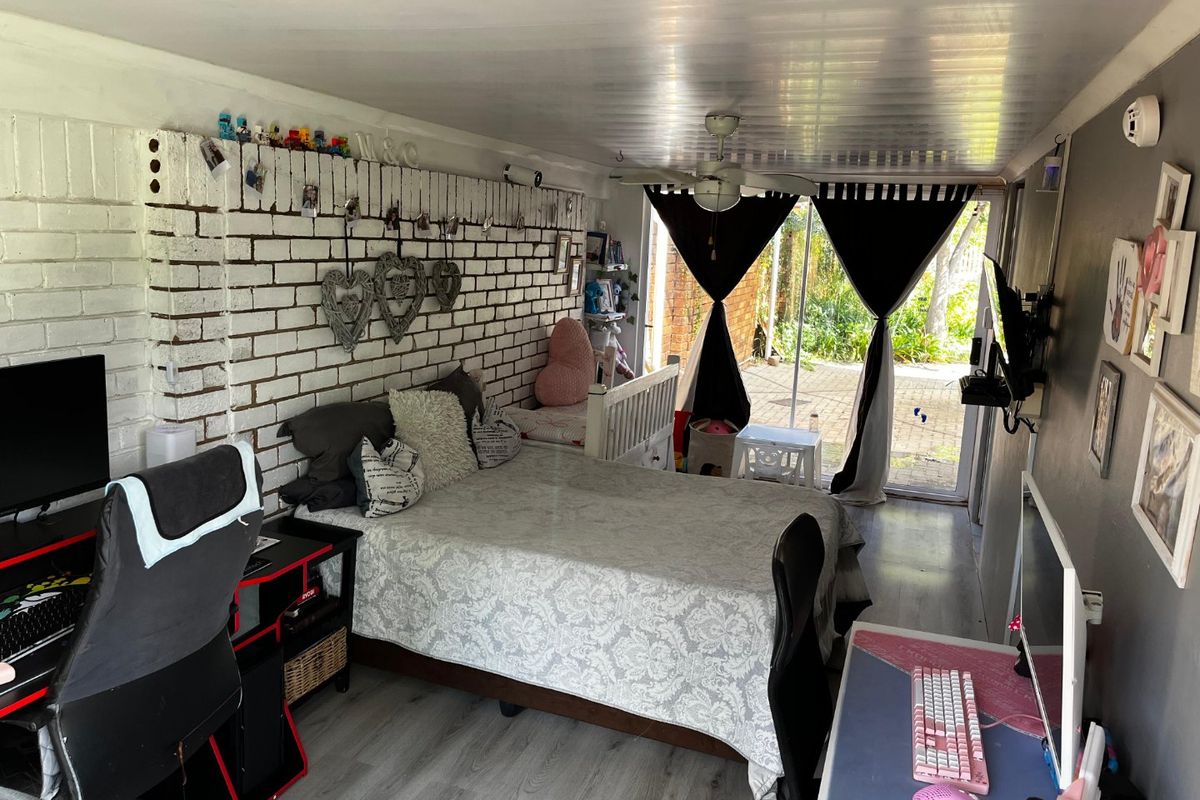 A bedroom featuring an exposed brick wall, ceiling fan, and sliding glass door providing access to the outdoor area.
