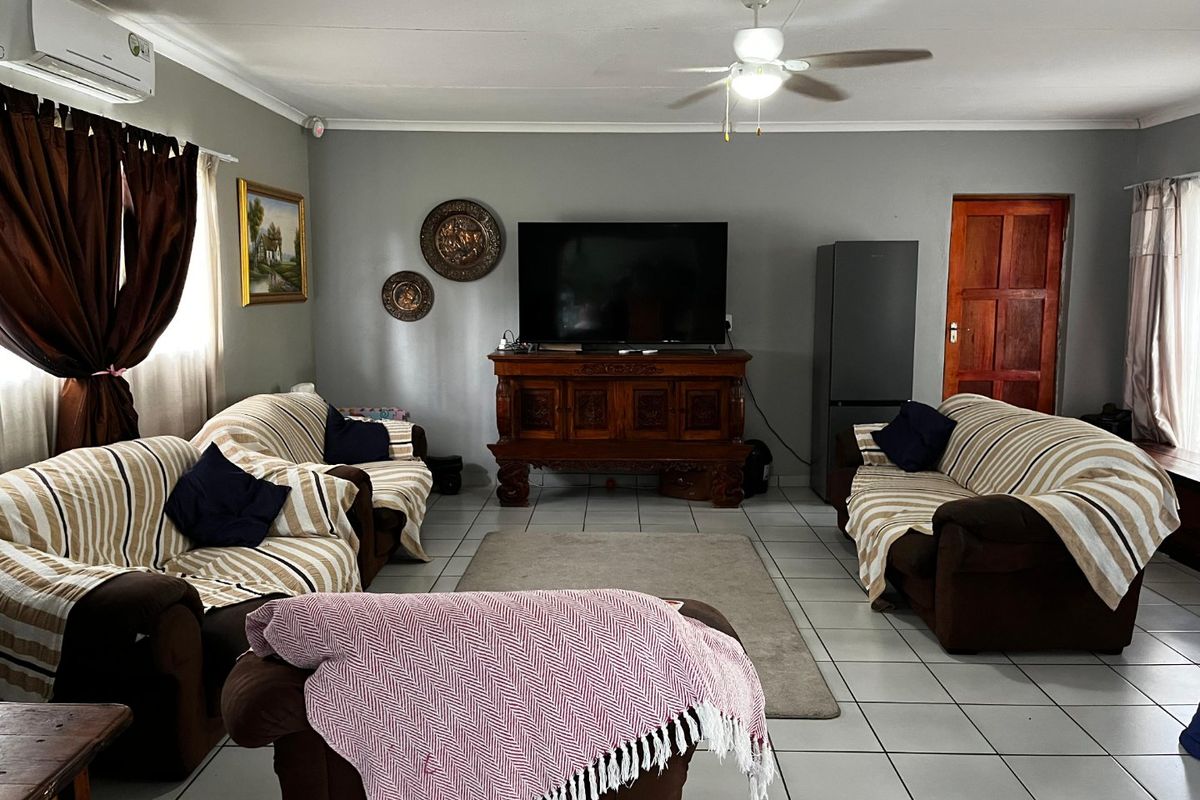 A spacious living room featuring tiled flooring, a ceiling fan, and a wall-mounted air conditioning unit, providing a comfortable and functional living space.