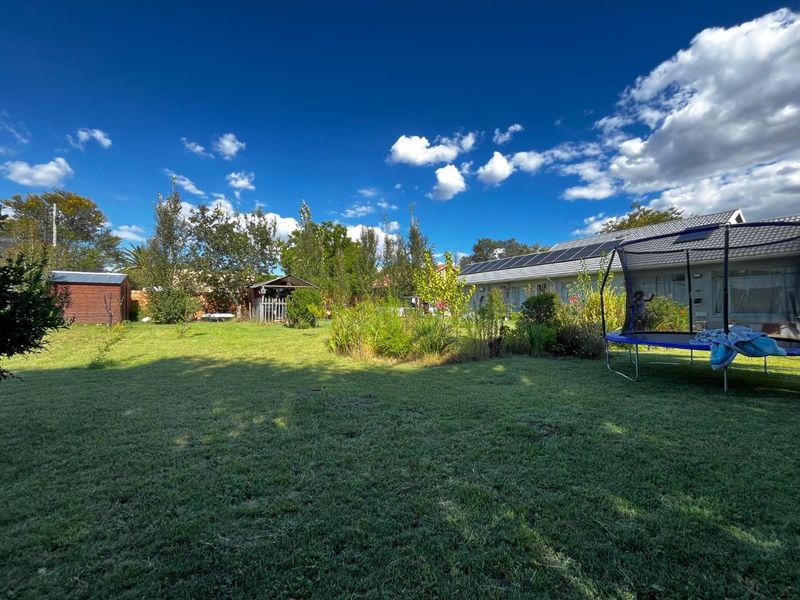A spacious rear garden featuring a well-maintained lawn, mature landscaping, a garden shed, and a house roof equipped with solar panels.