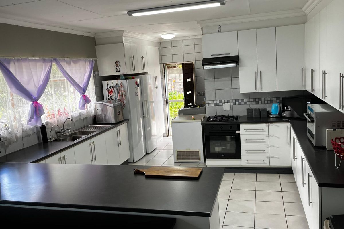 A functional kitchen featuring white cabinetry, dark countertops, a gas hob, and tiled flooring with direct access to the rear exterior.