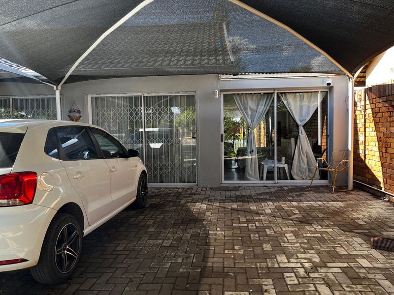 Paved front driveway area featuring a large shade sail, sliding glass doors with security gates, and brick boundary walling.