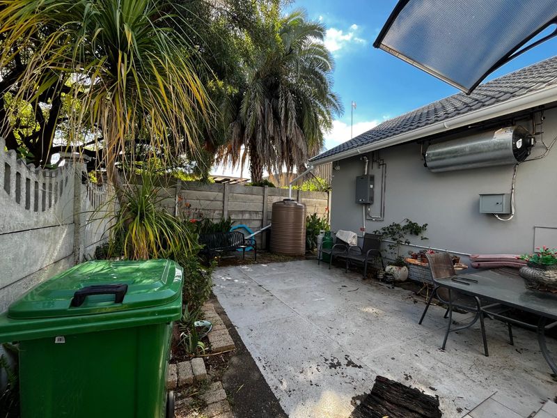 Rear exterior area featuring a concrete patio, boundary wall, and external water storage tank, providing a functional outdoor space.