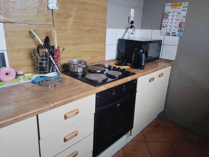 A functional kitchen area featuring a built-in oven, electric hob, laminate countertops, and tiled splashback with fitted cabinetry.
