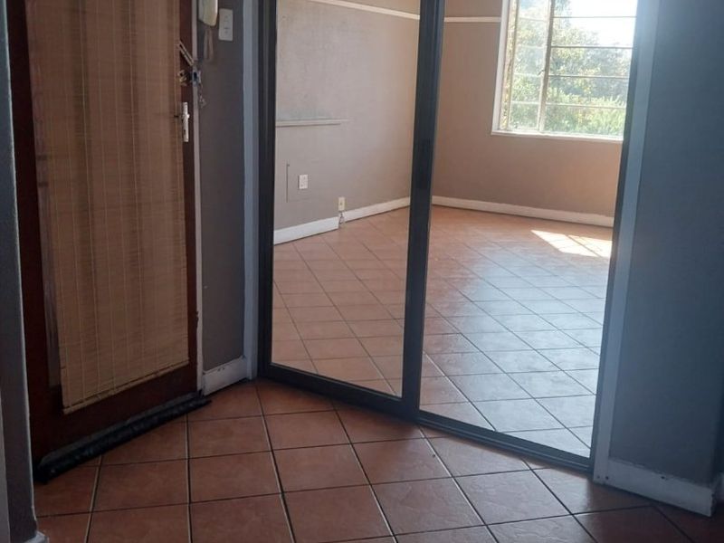 An entry area featuring tiled flooring, an intercom system, and a sliding glass door leading into an adjacent room with natural light.