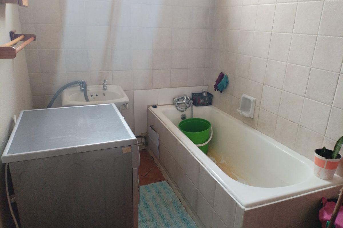 A functional bathroom featuring a bathtub, wall-mounted basin, and tiled finishes. The space requires cosmetic updates and maintenance to improve its overall condition.