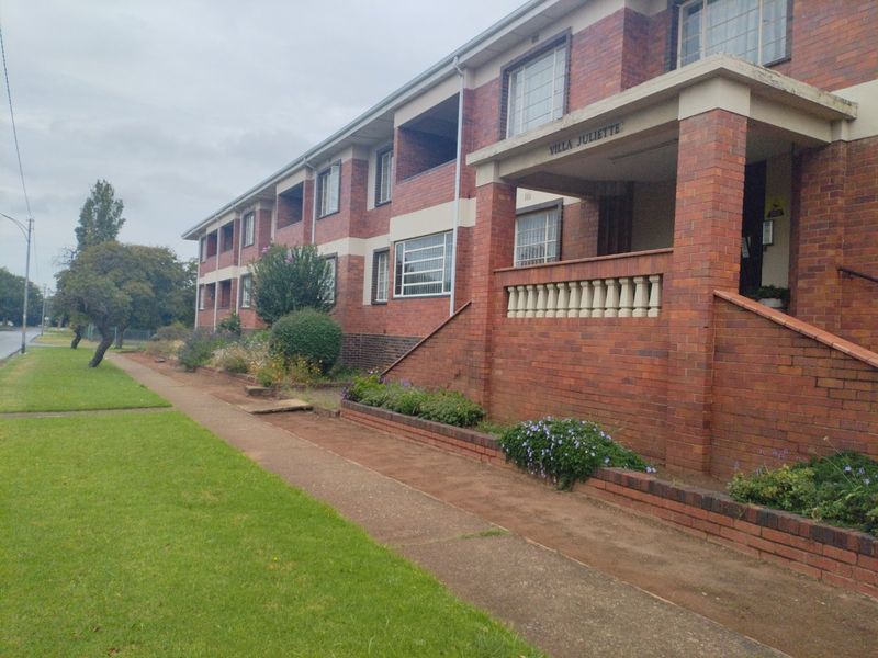 Exterior view of the Villa Juliette apartment complex featuring a classic red brick facade, covered balconies, and a paved front entrance walkway.
