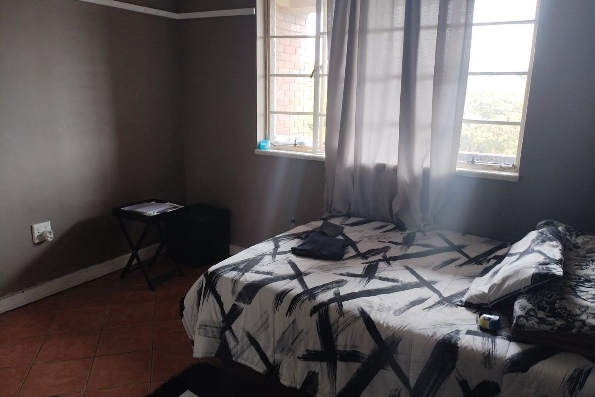 A bedroom featuring ceramic floor tiles, a steel-framed window, and neutral wall paint with a traditional picture rail.