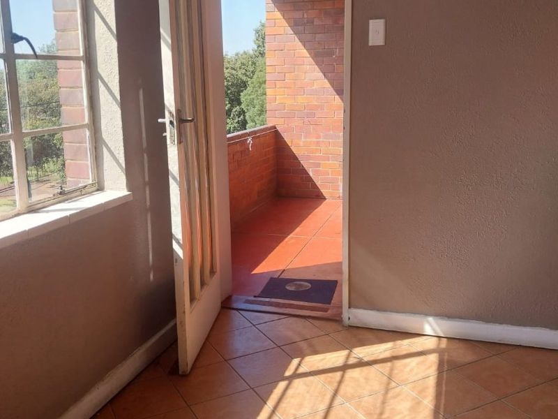An empty living area featuring tiled flooring and direct access to an outdoor balcony through a timber door.