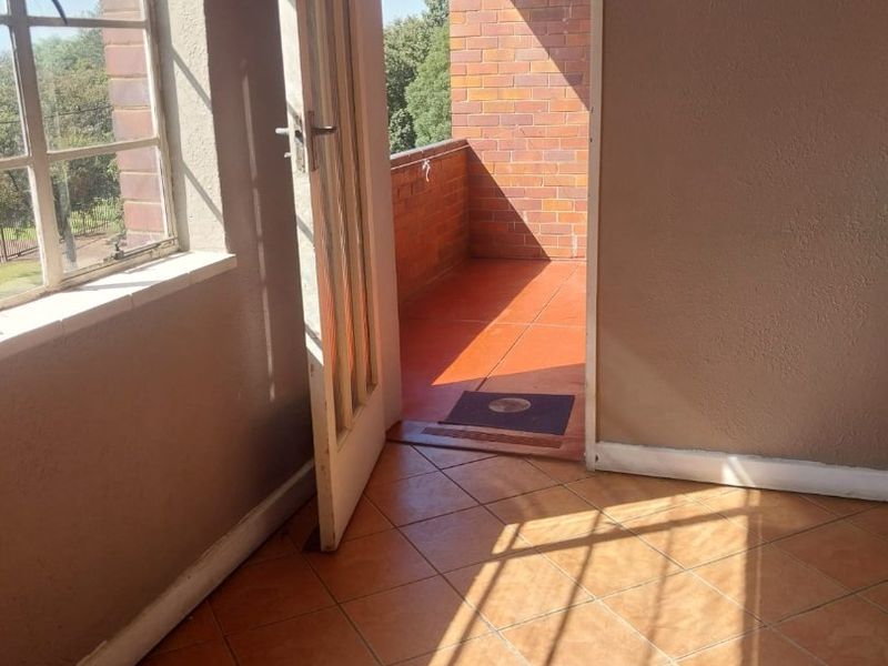 An empty living area featuring tiled flooring and direct access to an outdoor balcony through a timber-framed door.