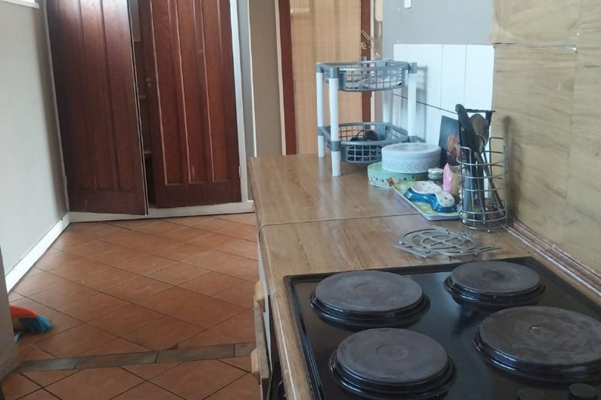 A functional kitchen area featuring a built-in electric hob, laminate countertops, and tiled flooring, requiring some cosmetic updates to the wall finishes.