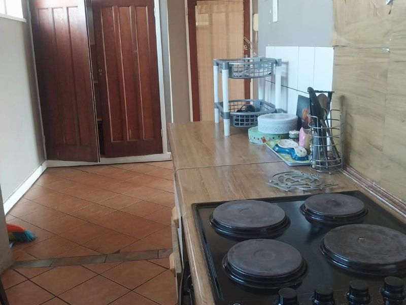 A functional kitchen area featuring a built-in electric hob, laminate countertops, and tiled flooring, requiring some cosmetic updates to the wall finishes.