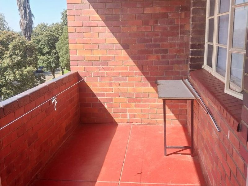 A simple, open-air balcony featuring exposed brick walls and a painted concrete floor, offering a functional outdoor space.