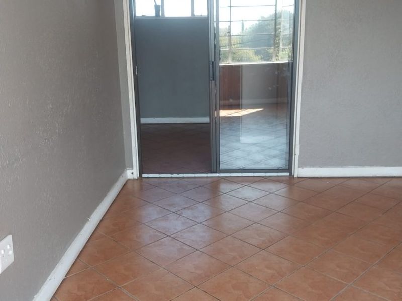 An empty living room featuring ceramic floor tiles and a sliding glass door leading to an adjacent space.