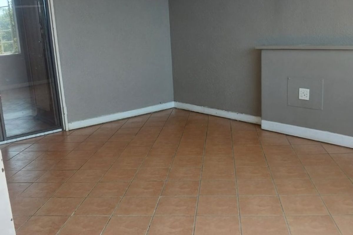 An empty living room featuring neutral grey walls, tiled flooring, and a glass sliding door providing natural light.