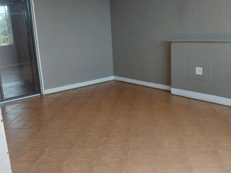 An empty living room featuring neutral grey walls, tiled flooring, and a glass sliding door providing natural light.