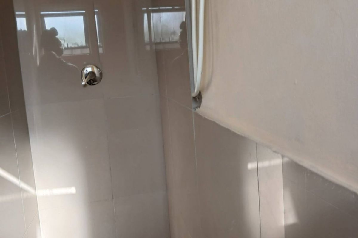 A compact bathroom featuring a shower enclosure with tiled walls and a wall-mounted basin, showing visible surface-mounted plumbing.