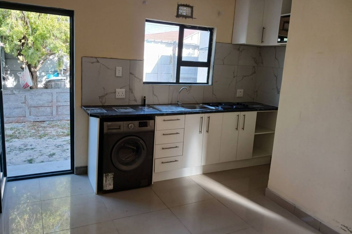 Compact kitchen featuring white cabinetry, dark laminate countertops, tiled backsplash, and direct access to an outdoor area through a sliding glass door.