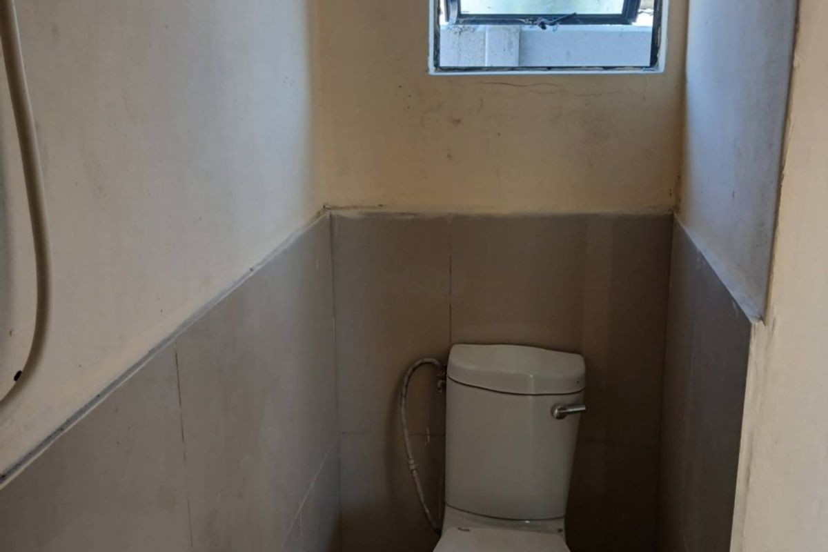 A compact bathroom featuring a toilet, small basin, and tiled finishes. The space requires cosmetic updates and repairs to the wall finishes.