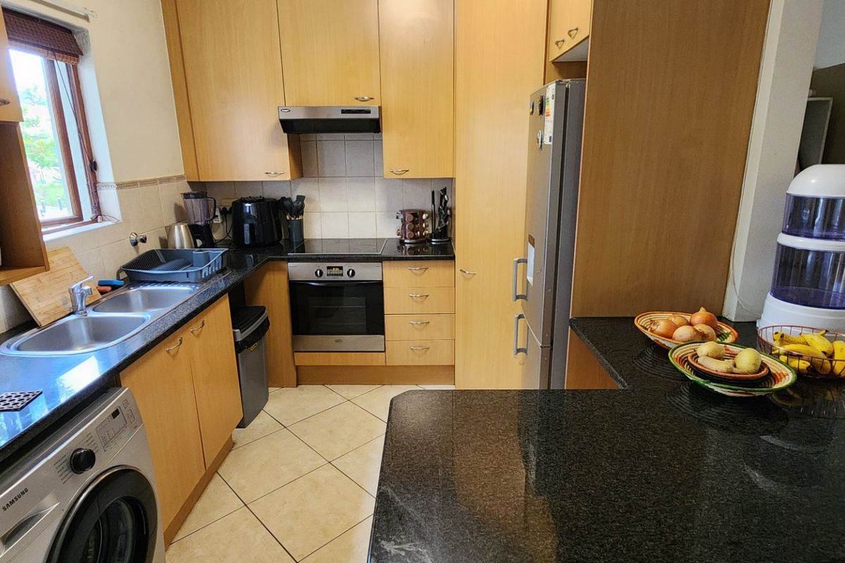 A functional kitchen featuring light wood cabinetry, dark granite countertops, a breakfast bar, and integrated appliances including an oven and hob.