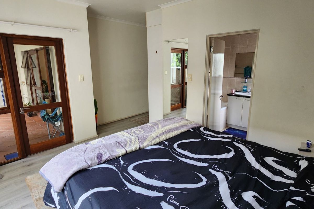 Spacious bedroom featuring laminate flooring, direct access to a private balcony, and an adjoining en-suite bathroom with a built-in vanity.