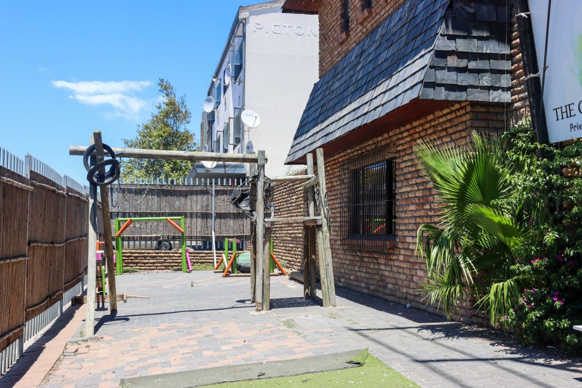 Exterior rear courtyard area featuring brick wall construction, slate roofing, and paved ground surface with security fencing and window bars.
