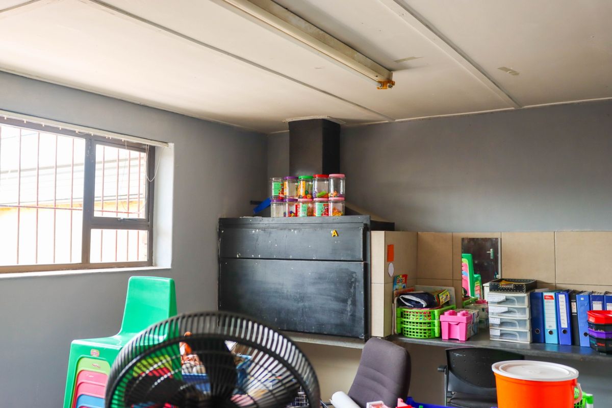 A functional kitchen area featuring a built-in extractor fan, tiled splashback, and security bars on the window, suitable for commercial or utility use.