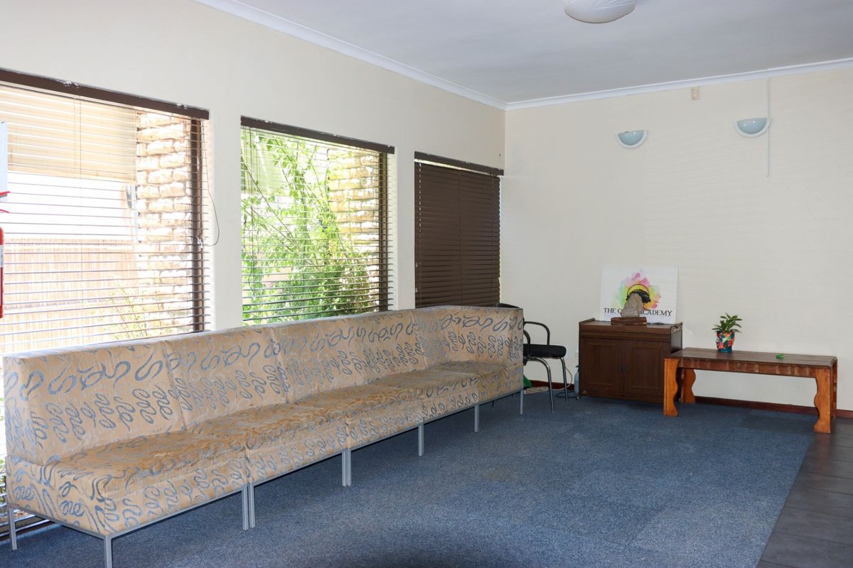 A spacious commercial waiting area or lounge featuring large windows with venetian blinds, carpeted flooring, and wall-mounted lighting.