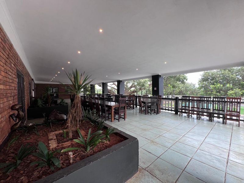 A spacious covered outdoor patio featuring tiled flooring, recessed lighting, and a built-in planter box, overlooking the garden area.