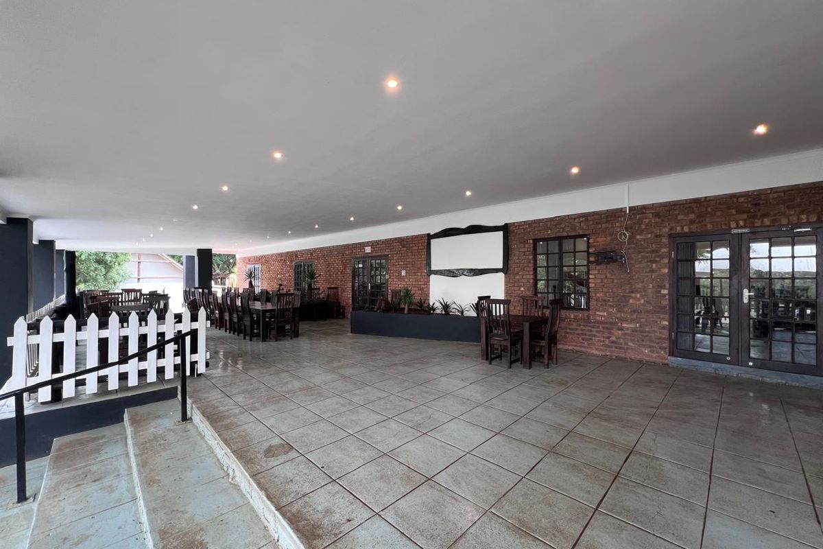 Spacious covered outdoor patio featuring exposed brick walls, tiled flooring, and recessed lighting, suitable for commercial dining or event use.