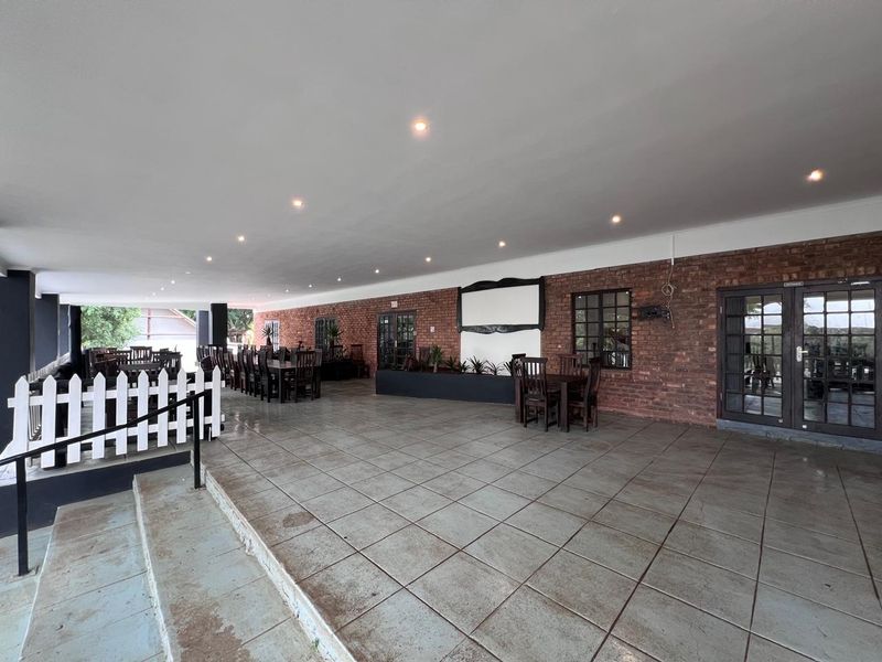 Spacious covered outdoor patio featuring exposed brick walls, tiled flooring, and recessed lighting, suitable for commercial dining or event use.