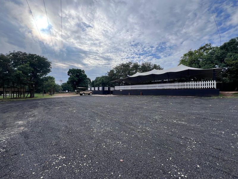 Spacious gravel parking area leading to a commercial outdoor entertainment space featuring a large tensioned fabric canopy and white picket fencing.