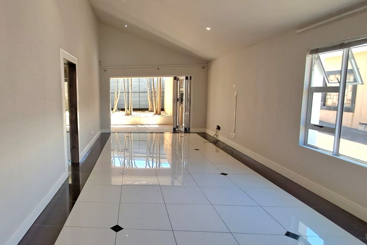 A bright, empty living room featuring high vaulted ceilings, modern porcelain floor tiles with decorative inlays, and bi-fold doors opening to an outdoor area.