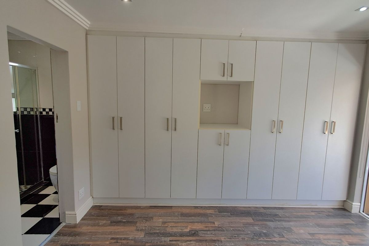A spacious bedroom featuring extensive built-in cabinetry, recessed lighting, and direct access to an en-suite bathroom and outdoor area.